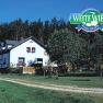 A white farmhouse with flowers in front of a forest, above it the logo 'Biohof Weite Wies Fam.
