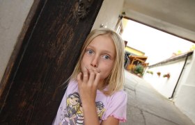 A girl stands in an archway and looks at the camera in surprise.