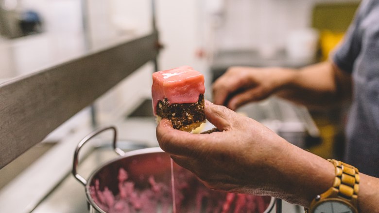 Person holding a piece of pastry with pink icing over a pot.
