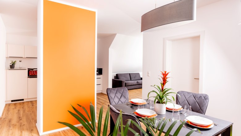 Modern apartment with dining area, orange wall and gray sofa.