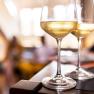 Two wine glasses with white wine on a table, blurred background.