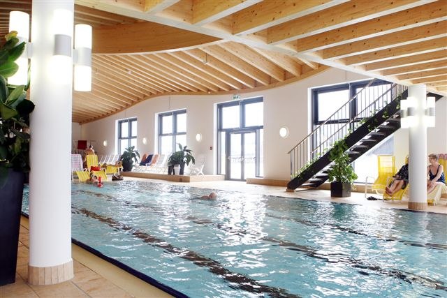 Interior view of a swimming pool with wooden ceiling and large windows.