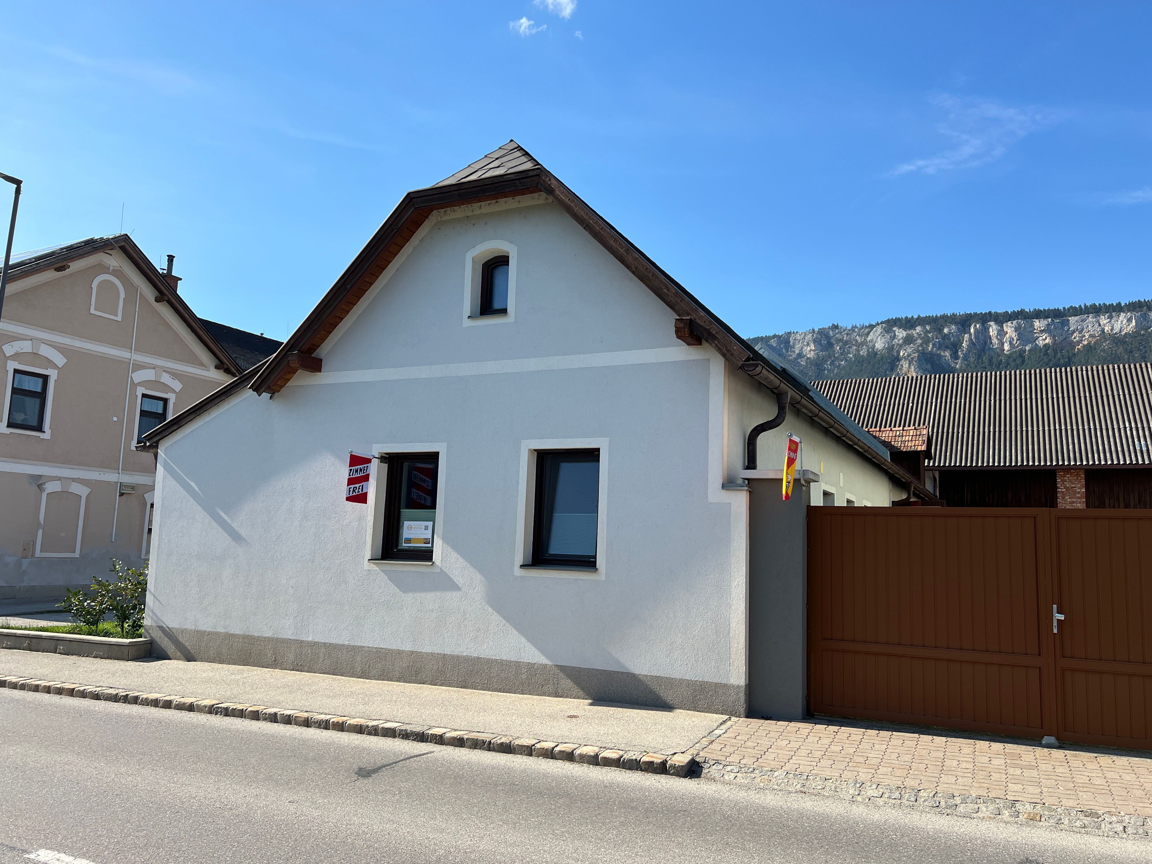 A small, white vacation home with a brown gate and a mountain backdrop.