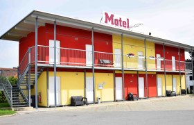 Two-story motel building with yellow and red walls, stairs and balcony.