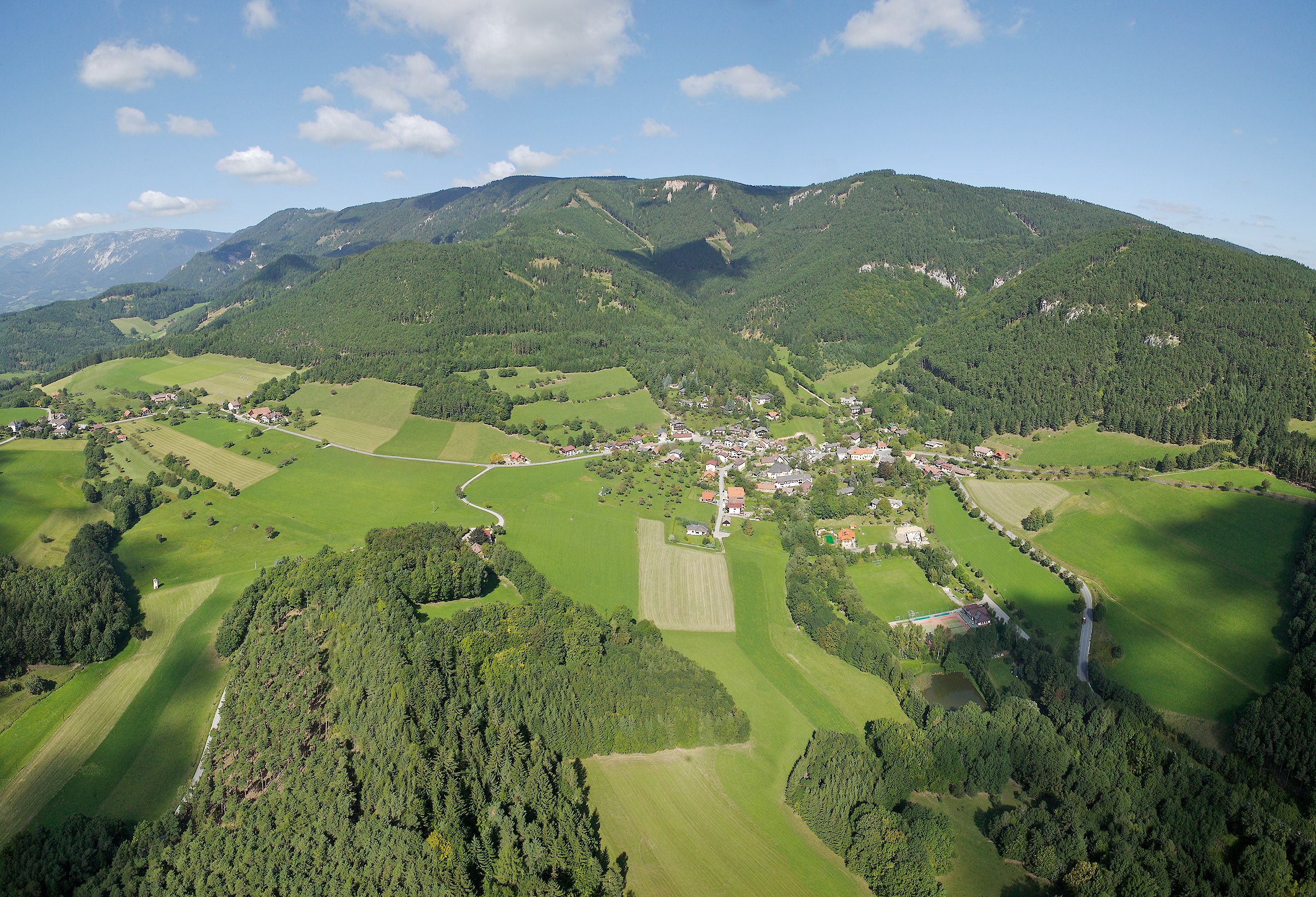 Aerial view of the municipality of Prigglitz with green fields and forests, surrounded by hills.