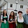 A family stands in front of a building labeled 'Haus Peilsteinblick'. They are wearing traditional clothing and holding bottles in their hands.