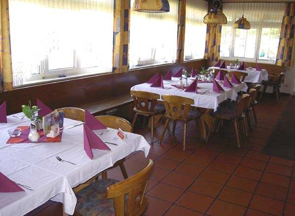 A dining room with laid tables, white tablecloths and purple napkins. Wooden chairs and large windows are visible.