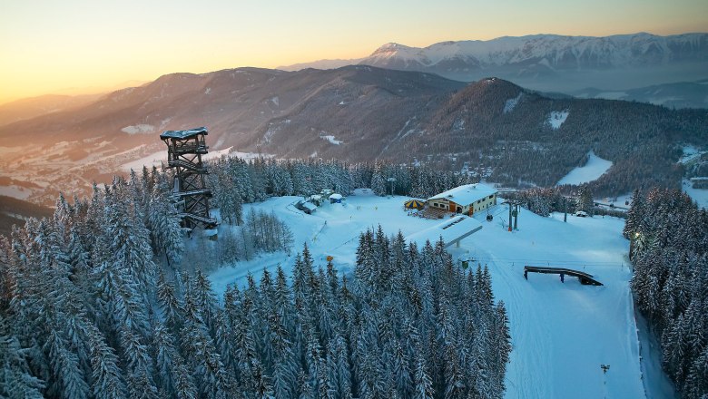 Winter landscape with observation tower and snow-covered trees at sunset.