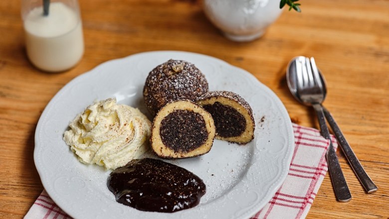 Plate with poppy seed dumplings, cream and chocolate sauce on a wooden table.