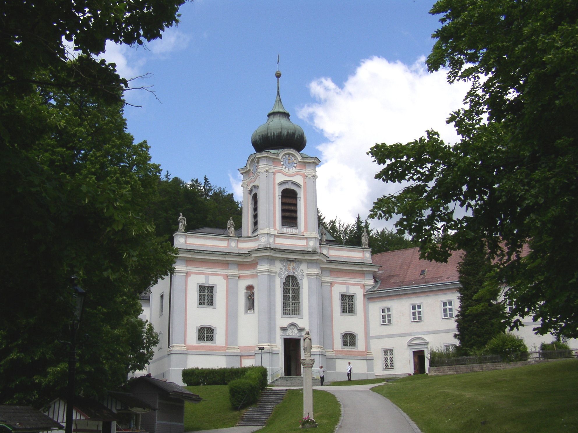 Baroque church on the Mariahilfberg with a green tower and surrounded by trees.