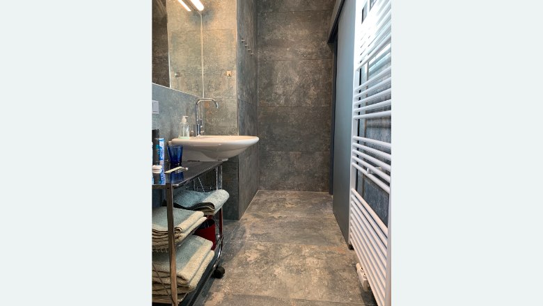 Modern bathroom with gray tiles, washbasin, towel rack and radiator.