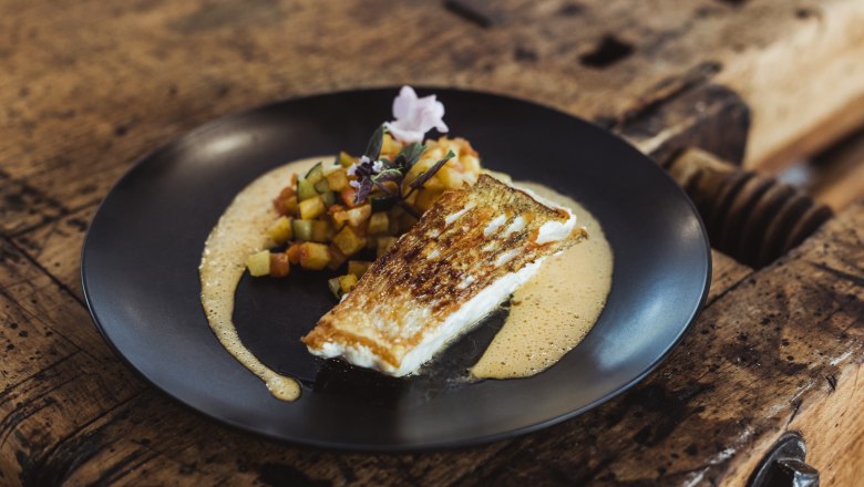 Fried fish with diced vegetables and sauce served on a black plate.