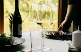 A laid table with a bottle of wine, wine glasses and a plate of food in a restaurant.