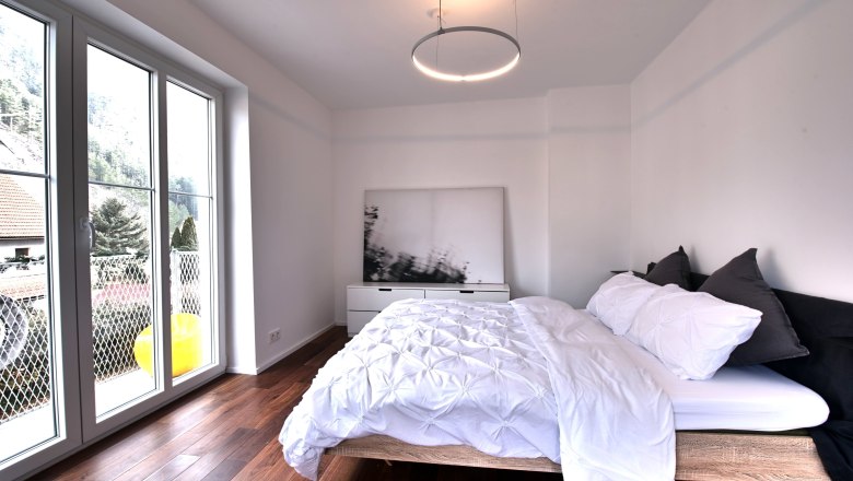 Modern bedroom with large window, wooden floor and double bed.