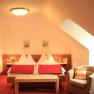 A cozy double room with two beds, red blankets, an armchair and a table under a sloping roof.
