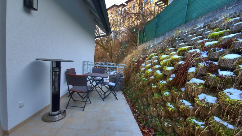 Terrace with table, chairs and radiant heater next to a green wall.
