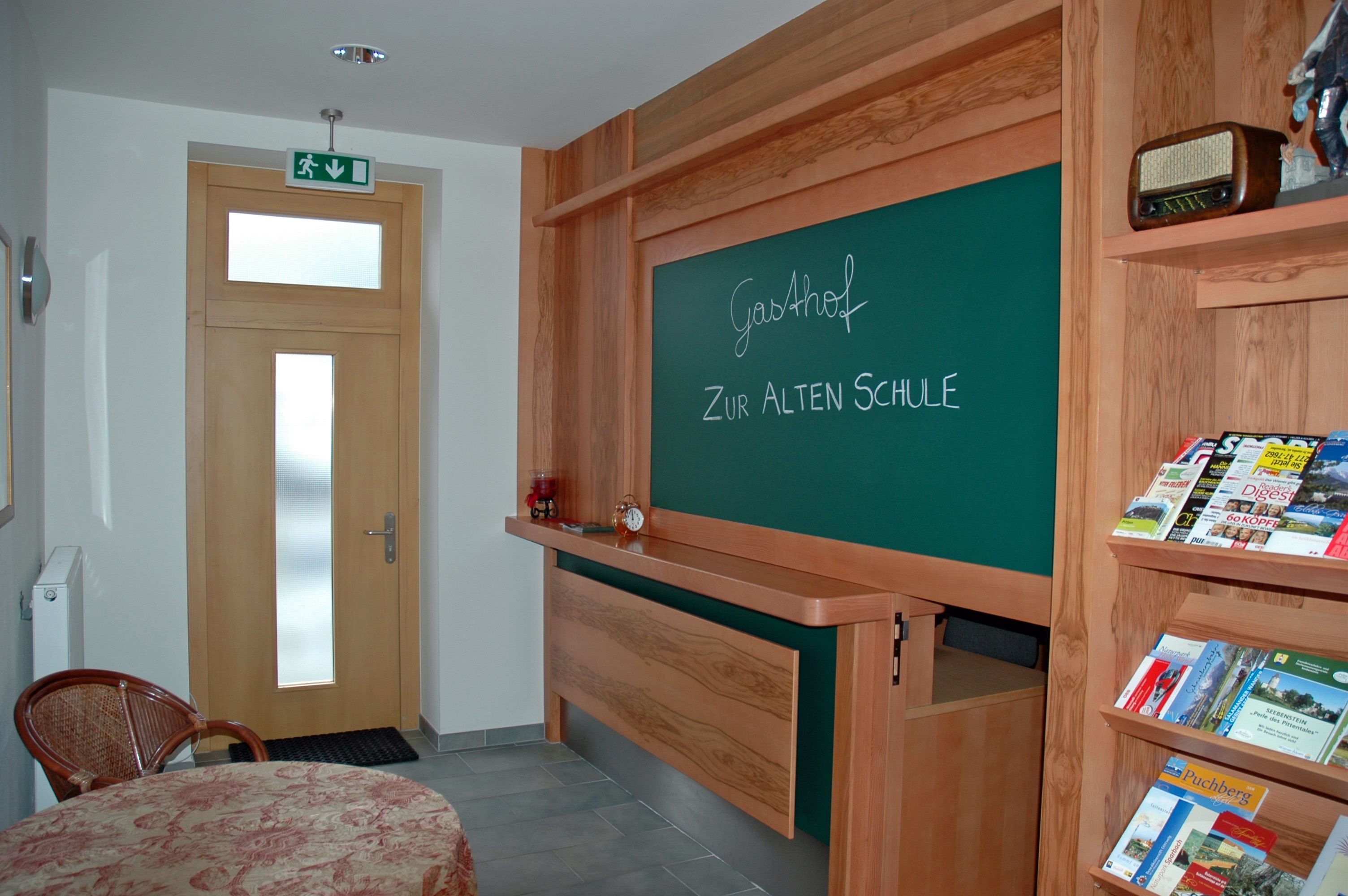 Interior view of a hotel with a board reading 'Gasthof Zur Alten Schule' and a shelf with brochures.
