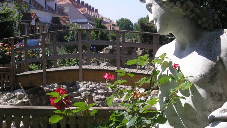 Stone statue next to a wooden bridge and red roses in the foreground.
