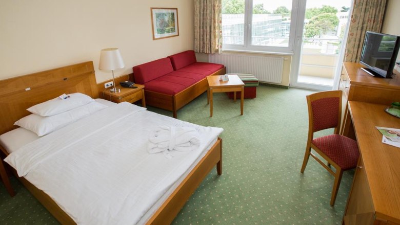 Hotel room with double bed, red sofa, desk and balcony.