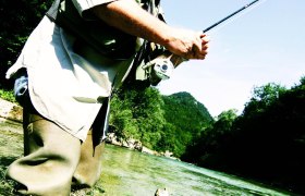 A man fly fishing in a river, with a jumping fish in the foreground.