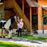 A woman stands next to a black and white horse in front of a wooden building.