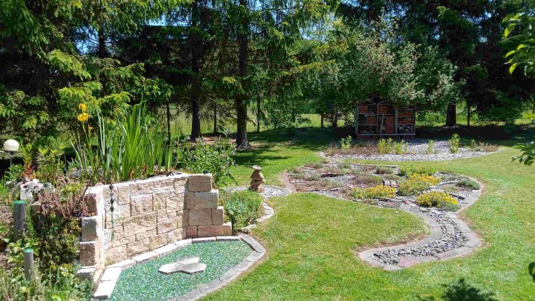 A well-tended garden with stones, plants and an insect hotel in the background.
