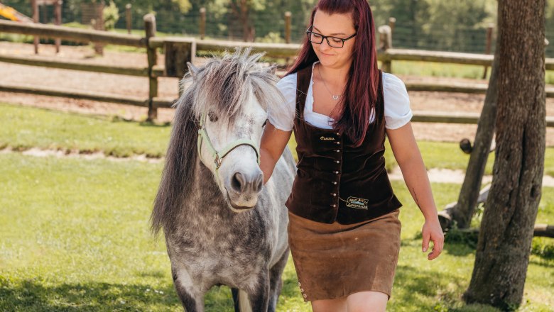 Claudia Langthaler leads a pony in a meadow, with a wooden fence in the background.