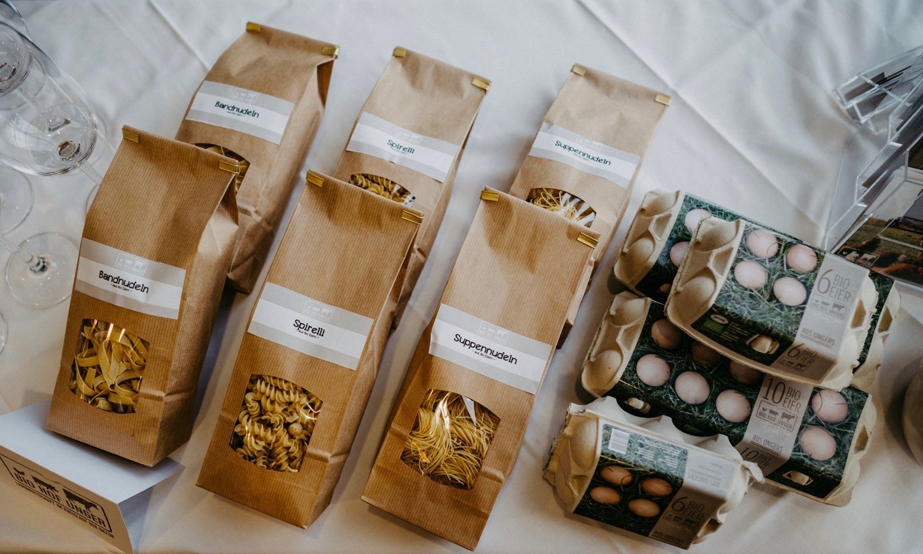 Products from Biohof Unger: pasta in brown bags and egg cartons on a table.