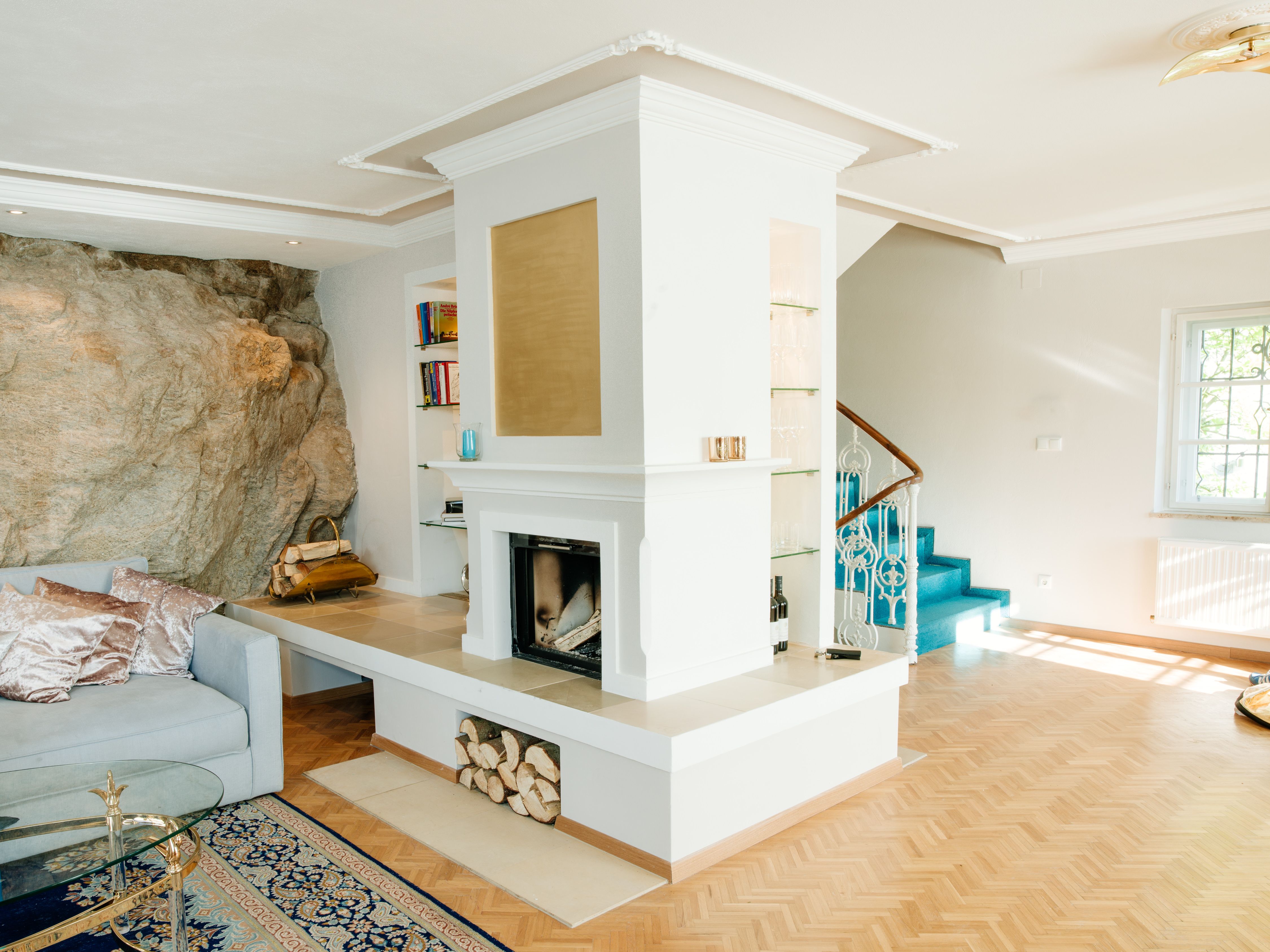 Living room with fireplace, rock wall, blue staircase and wooden floor.