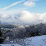 Winter landscape with snow-covered trees and hills under a blue sky with clouds.