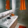 Modern bathroom with double washbasin, large mirror, shower and orange accents.