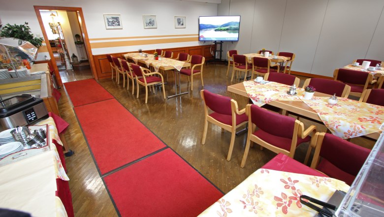A conference room with covered tables, red chairs and a large screen.