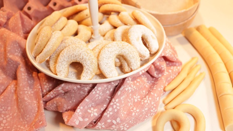 A plate of vanilla crescents on a pink cloth, surrounded by rolls of dough.