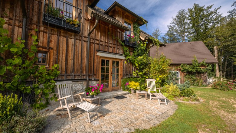 Wooden house with terrace and garden furniture, surrounded by plants.