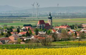 View of Pillichsdorf with church, surrounded by fields and wind turbines in the background.