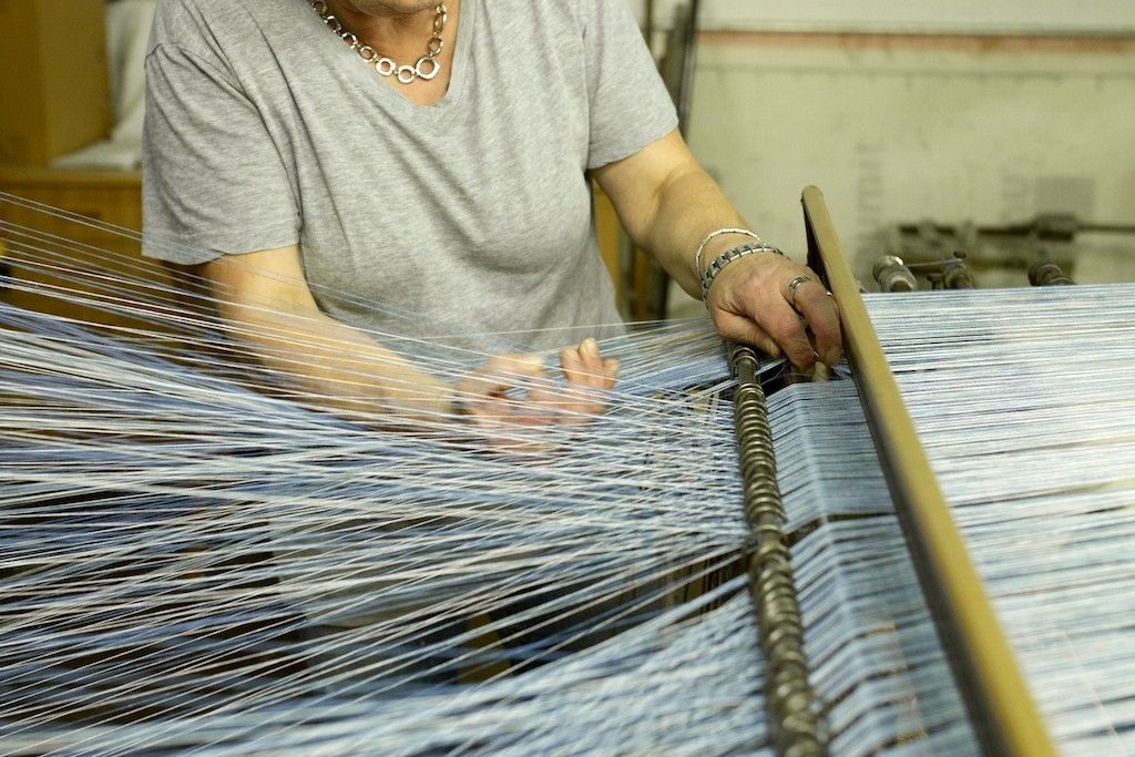 Person working on a loom with blue threads.