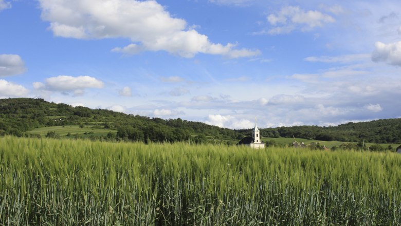 Landscape with green field, church in the background and blue sky with clouds.