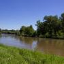 River with green banks and trees under a clear blue sky.