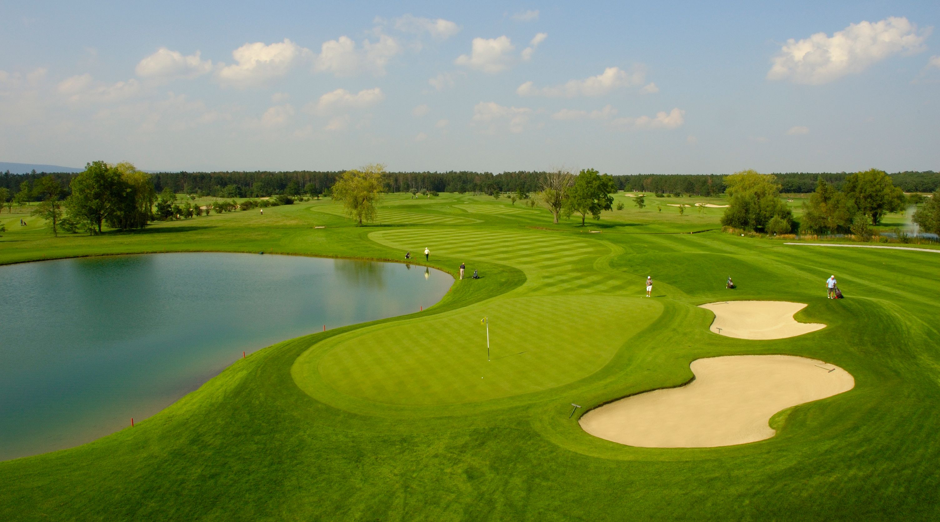 Golf course with pond, sand bunker and players.