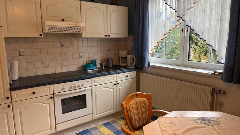 Kitchen with white cupboards, stove, sink and window with curtains.
