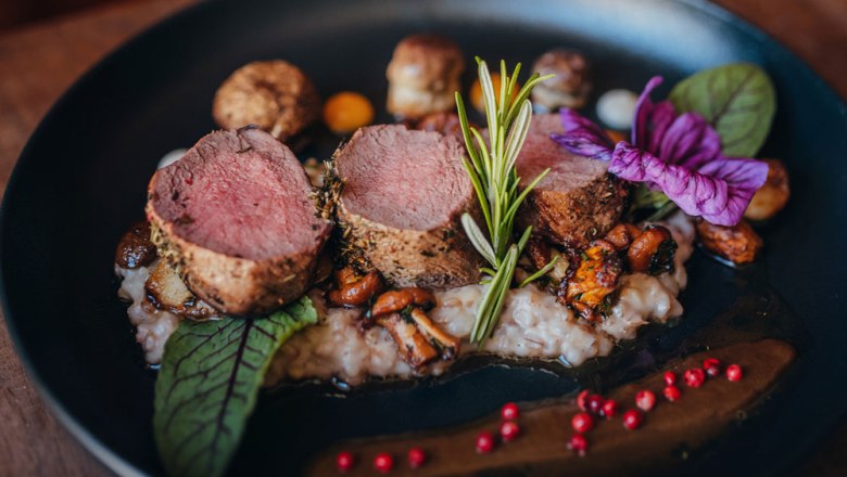 Pink roasted venison steak on risotto decorated with rosemary and flowers.