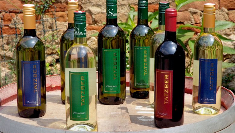Various Tatzber wine bottles on a barrel in the open air.