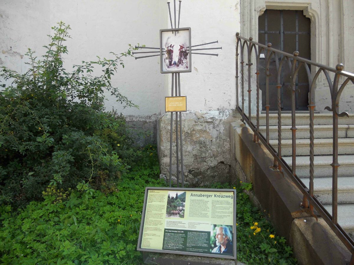 A sign with information about the Annaberg Way of the Cross next to a staircase and plants.