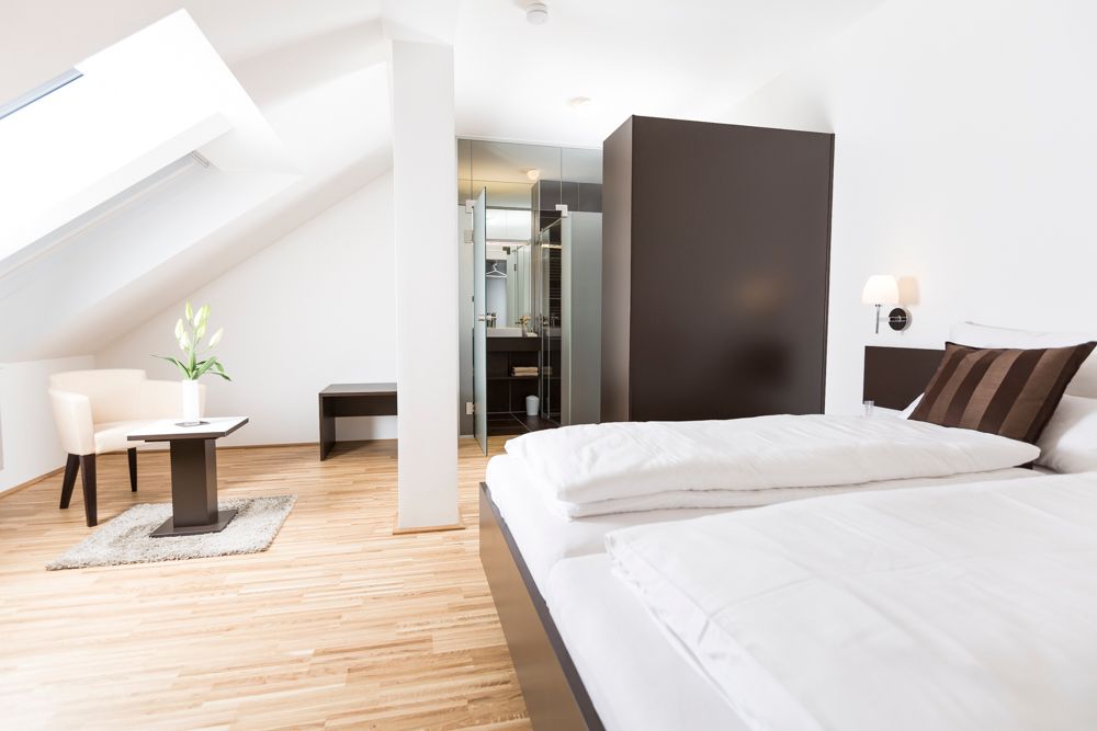 Modern guest room with bed, armchair and table under a sloping roof.