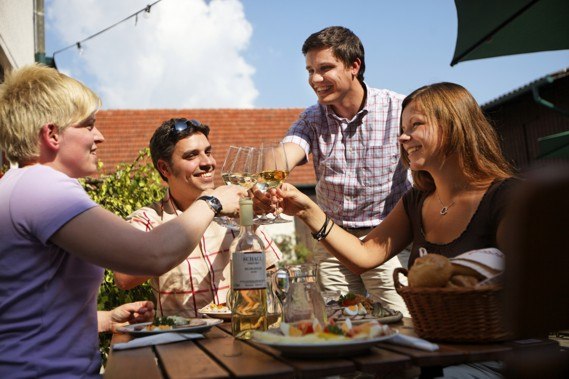 Four people clink glasses of wine at an outdoor table.