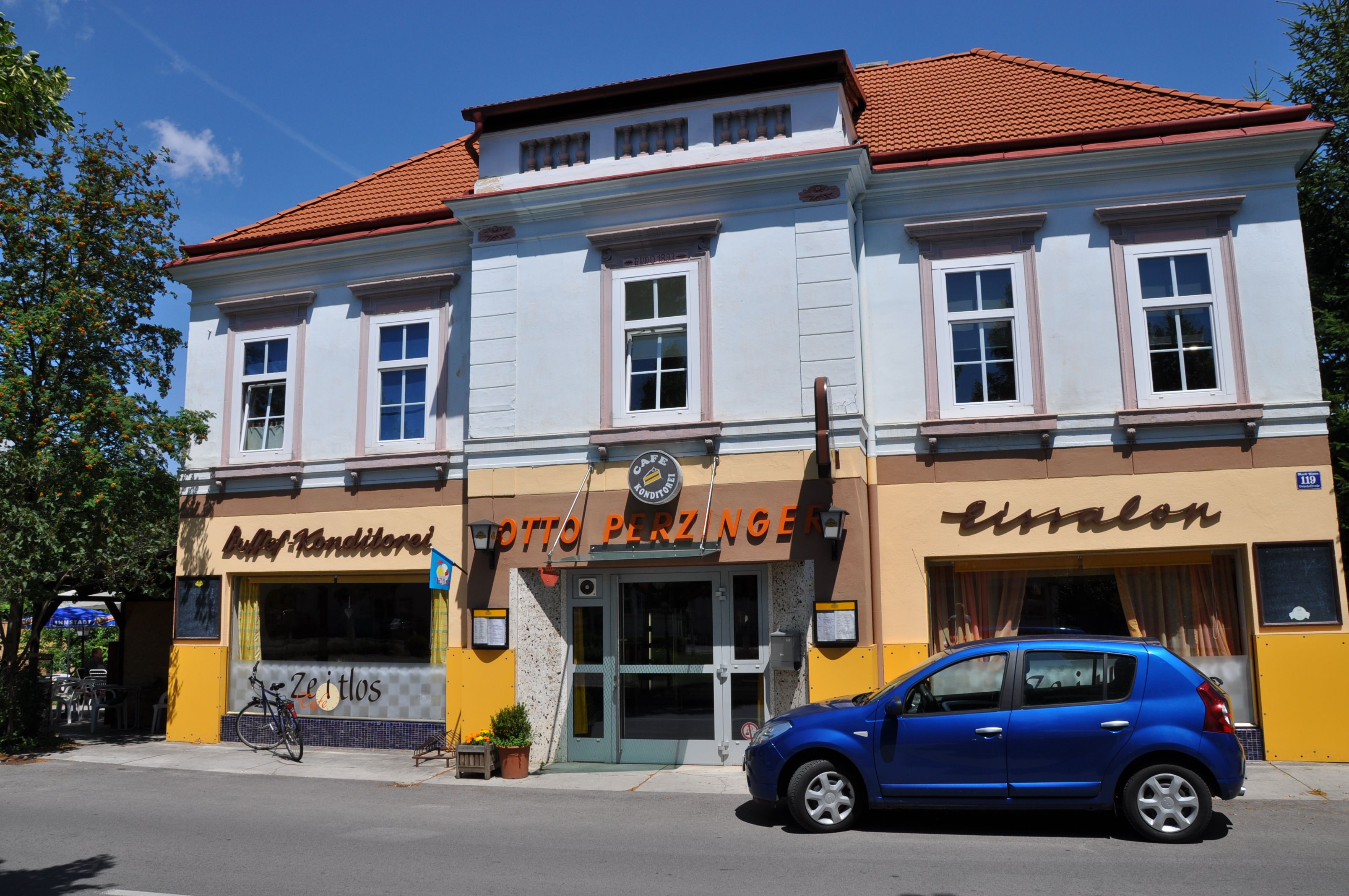 Exterior view of a café with a blue façade and red roof, a blue car parked in front of it.