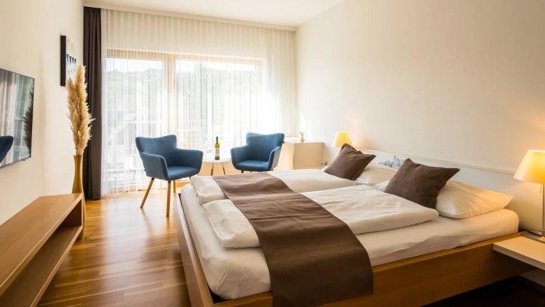 Modern guest room with double bed, blue armchairs and wooden floor.