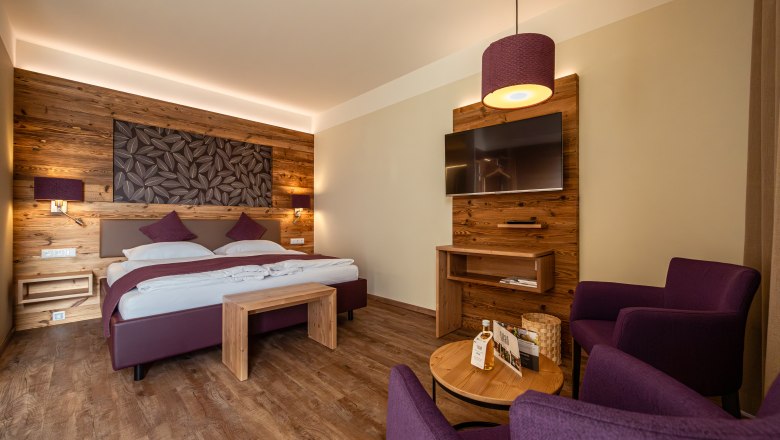 Cozy hotel room with wooden walls, double bed, TV and purple armchairs.