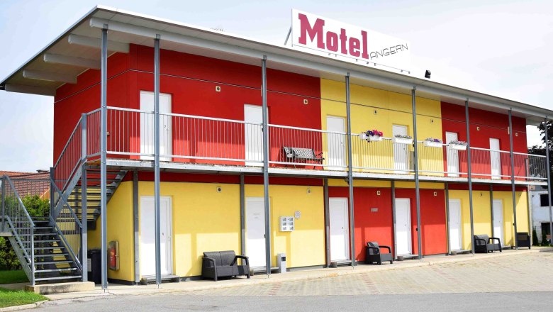Two-story motel building with yellow and red walls, stairs and balcony.