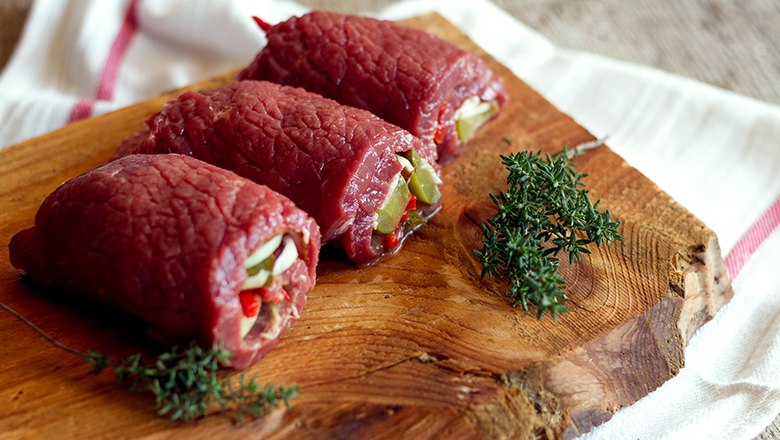 Three stuffed raw beef roulades on a wooden board with sprigs of thyme.